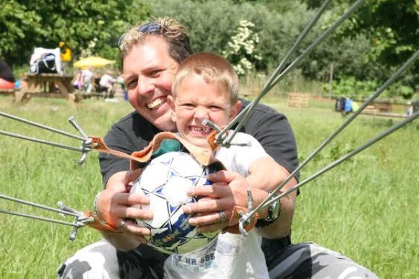 Vader en zoon met katapult en voetbal tijdens uitje