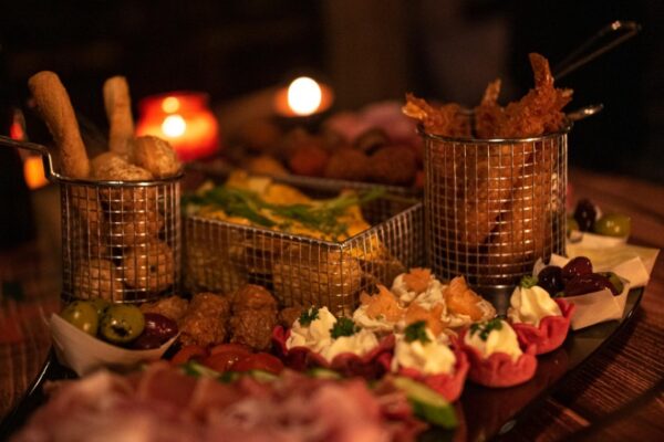 winterborrel-hapjes-close-up - Outdoorpark SEC Almere Close-up van een feestelijke winterborrelplatter met diverse gourmet snacks, gefrituurde garnalen en olijven, sfeervol verlicht door kaarslicht.
