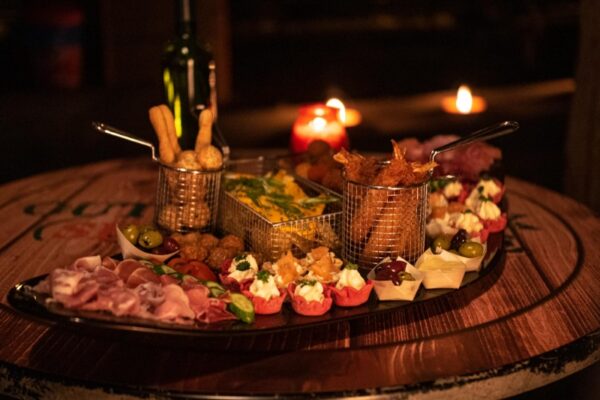 winterse-borrelplank-catering - Outdoorpark SEC Almere Diverse winterse borrelhapjes en snacks op een houten tafel, sfeervol verlicht met kaarsen, voor een gezellige winterborrel.