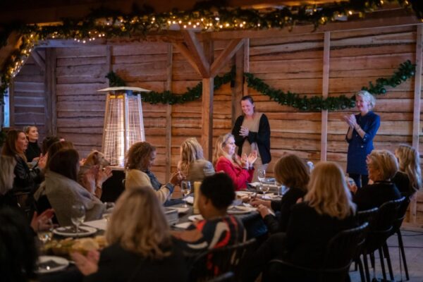 zakelijke-winterborrel-evenement - Outdoorpark SEC Almere Groep vrouwen klapt en luistert tijdens een sfeervolle zakelijke winterborrel of bedrijfsfeest in een rustieke, verwarmde setting.