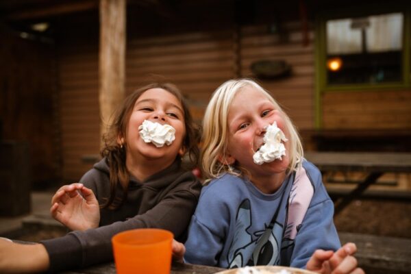 blije-kinderen-slagroom-gezichten-schoolreisje-outdoorpark-almere - Outdoorpark SEC Almere Twee lachende kinderen met slagroom op hun gezicht genieten van een grappig moment tijdens een schoolreisje pauze bij Outdoorpark Almere.