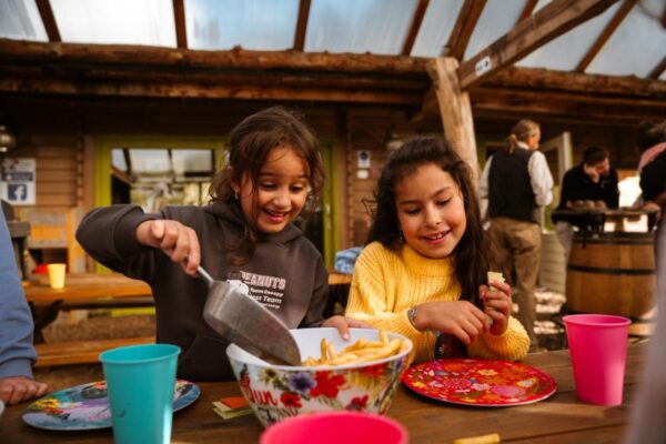 kinderen-eten-patat-buiten-schoolreisje-outdoorpark-almere - Outdoorpark SEC Almere Twee blije kinderen delen patat aan een buitentafel tijdens een schoolreisje maaltijd bij Outdoorpark Almere.