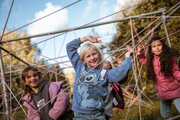 kinderen-navigeren-spinnenweb-parcours-schoolreisje-teambuilding - Outdoorpark SEC Almere Lachende kinderen navigeren een speels spinnenweb parcours van touwen tijdens een teambuilding schoolreisje.
