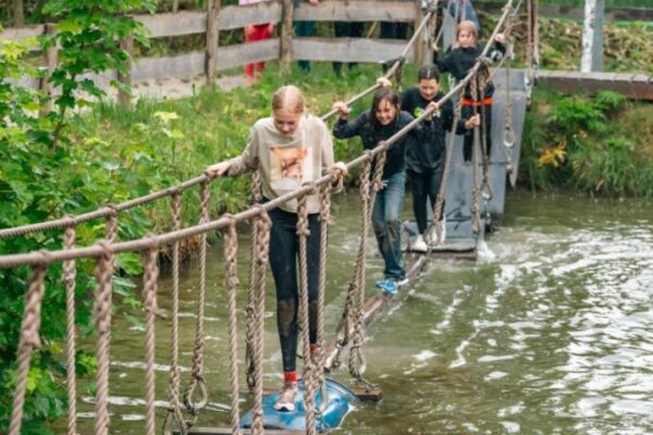 kinderen-oversteken-junglebrug-water-survival - Outdoorpark SEC Almere Kinderen steken een junglebrug over met tonnen en touwen over het water