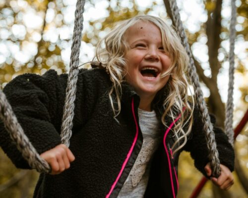 lachend-kind-survival-schoolreisje-outdoorpark-almere - Outdoorpark SEC Almere Lachend blond kind op een survival parcours met touwen, genietend van een actieve schoolreis in Outdoorpark SEC Almere.