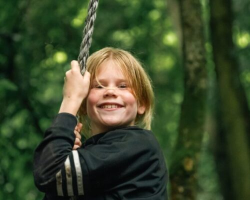 lachend-kind-touwklimmen-survival-schoolreisje-outdoorpark-almere - Outdoorpark SEC Almere Lachend kind houdt een touw vast tijdens een actief survival schoolreisje bij Outdoorpark SEC Almere, perfect voor klimmen en avontuurlijke uitjes