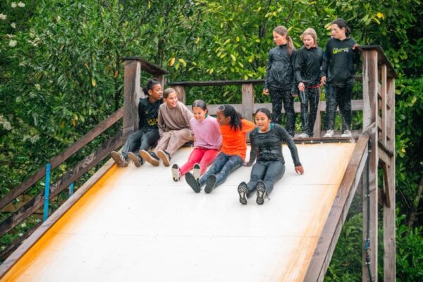 meisjes-waterswing-glijbaan-survival-schoolreisje - Outdoorpark SEC Almere Groep meisjes lacht en glijdt van de waterswing tijdens survival schoolreisje
