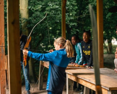 schoolreisje-boogschieten-kind-outdoorpark-almere - Outdoorpark SEC Almere Meisje leert boogschieten tijdens een actief schoolreisje bij Outdoorpark SEC Almere, een leuke en uitdagende outdoor activiteit voor kinderen en scholen.
