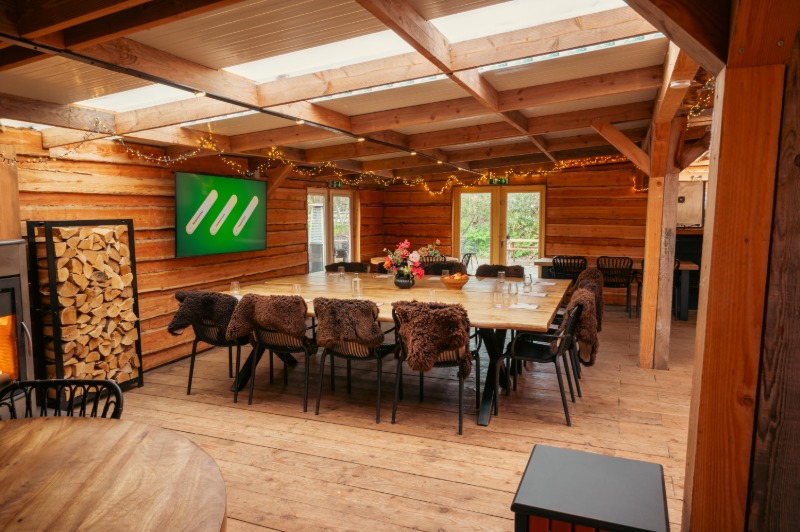 boshut-vergaderruimte-almere-grote-tafel - Outdoorpark SEC Almere Sfeervolle vergaderruimte in de Boshut bij Outdoorpark SEC Almere met lange houten tafel en moderne presentatiescherm