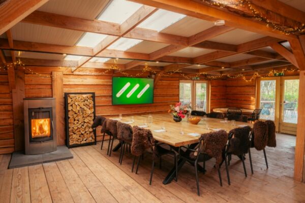 Sfeervolle Boshut meeting room at Outdoorpark Almere with a fireplace, large wooden table, and modern presentation screen.